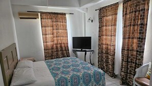 A bedroom with a bed, a television, curtains, and a chair. - Cozy Apartments close to beach, bars and restaurants (Rodney Bay)