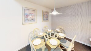 A dining area with a round glass table, six chairs, and two framed artworks on the wall. - Golf Villa | Sunset Beach | Live the Golf Life! (CV2B) (Sunset Beach)