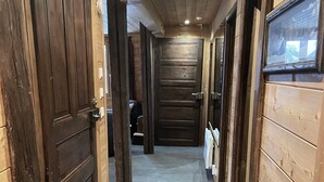 Un estrecho pasillo con paredes y puertas de madera, que conduce a una habitación con un ventanal grande.