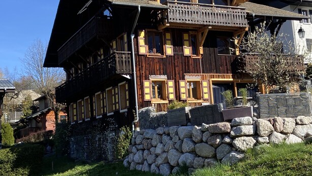 Una cabaña de madera de varios pisos con balcones, cimientos de piedra y un paisaje montañoso de fondo.