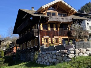 En flervånings chalet i trä med balkonger, en grund av sten och en bergig bakgrund.