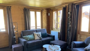 Un interior de cabaña acogedor con un sofá, dos sillones, una mesa de centro y piso de madera.