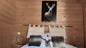 Un dormitorio de cabaña de madera con una cama decorada con almohadas con motivos de ciervo y un cartel grande de ciervo en la pared.