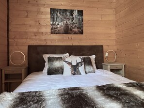 Ett sovrum i en stuga med träpanel, inrett med en säng, två sängbord och en tavla med ett motiv av rådjur som hänger på väggen.
