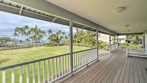 A covered wooden deck with a railing, overlooking a grassy area with palm trees and a view of the ocean. - Hilo Oasis - 32 Mi to Volcanoes National Park (Hilo)