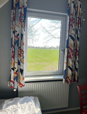Een kamer met een raam, een radiator eronder en een bed met witte lakens.