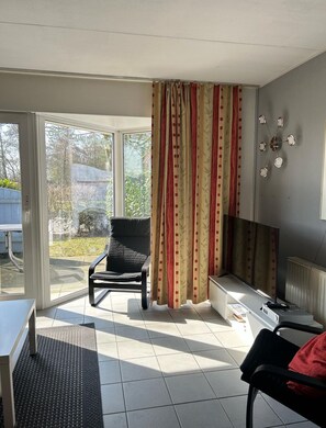 Quarto com porta de vidro deslizante para um jardim, uma cadeira preta, uma televisão e um radiador.