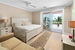 A bedroom with a bed, a nightstand, a lamp, a ceiling fan, a balcony with a view of the ocean, and a rug on the floor. - Directly on the Beach. Peaceful and Relaxing. (Nassau)