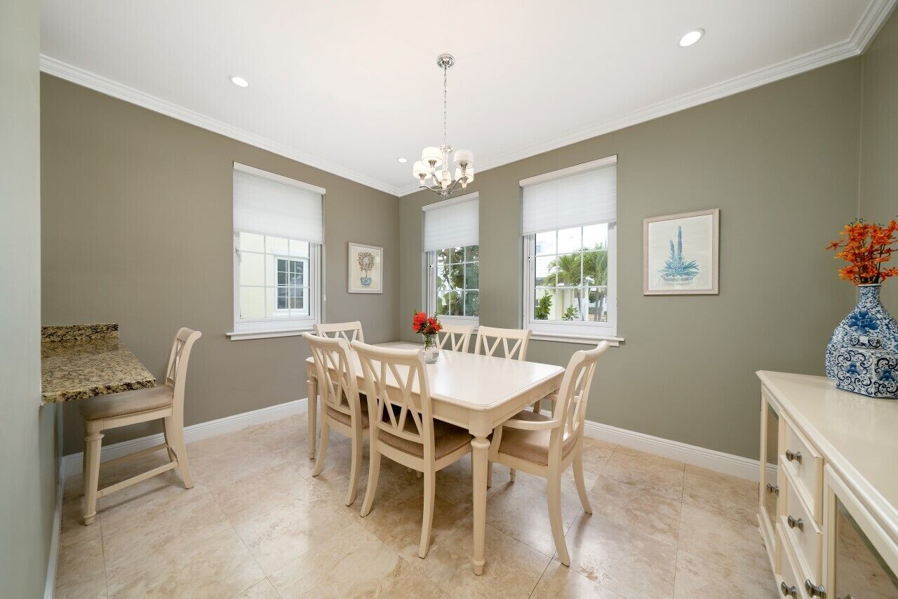 Une salle à manger avec une table et des chaises de couleur beige, de grandes fenêtres et un lustre.