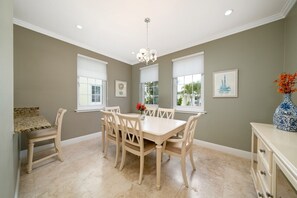 A dining room with a beige table and chairs, large windows, and a chandelier. - Directly on the Beach. Peaceful and Relaxing. (Nassau)
