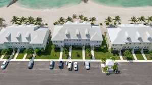 A beachfront hotel with three-story buildings, a parking lot, and a sandy beach with palm trees. - Directly on the Beach. Peaceful and Relaxing. (Nassau)