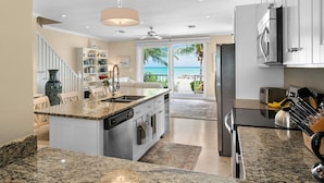 A modern kitchen with granite countertops, stainless steel appliances, and a view of the ocean through large sliding doors. - Directly on the Beach. Peaceful and Relaxing. (Nassau)