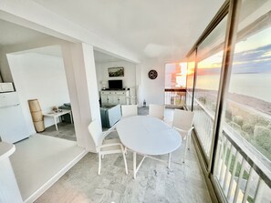 Een balkon met een witte tafel en stoelen, een keuken op de achtergrond en uitzicht op de zonsondergang over het water.