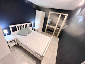 Een slaapkamer met een bed, nachtkastje, dressoir en een raam met uitzicht.