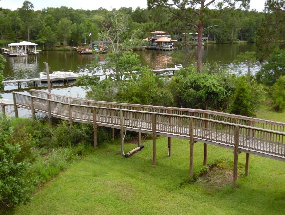Eine Holzbrücke über einem See mit Anlegestellen und Booten, umgeben von Grün.