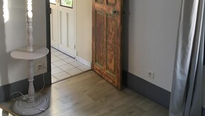 Ein Zimmer mit Holztür, einer weißen Lampe, einem Regal mit kleinen Pflanzen und einem grauen Vorhang.