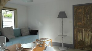 Ein Zimmer mit einem Holzespeisetisch, einer Couch mit Kissen, einer Stehlampe und einer großen Holztür.