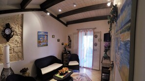 A living room with a stone wall, a black sofa, a coffee table with flowers, a clock, and a painting. - La Rosa dei Venti - Typical, Independent with Exclusive Terrace at150 mt from the Sea (Marina di Ragusa)