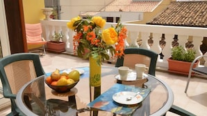 A round glass table with chairs, a bowl of fruit, a vase with flowers, and a plate with a spoon on a balcony. - La Rosa dei Venti - Typical, Independent with Exclusive Terrace at150 mt from the Sea (Marina di Ragusa)