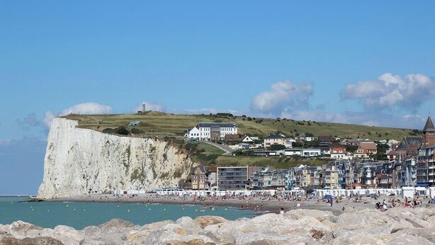 A coastal town with a prominent cliff, beach, and buildings along the shore.