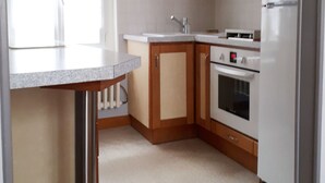 A kitchen with wooden cabinets, a white refrigerator, a microwave, and a clock on the wall.
