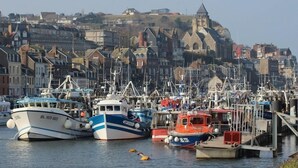 A harbor with boats docked, a church on a hill, and a town with historic buildings.