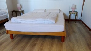 A neatly made bed with a white duvet and pillows, two bedside tables with lamps, and a wooden floor. - Beautiful house with its feet in the water, the sea at the end of the garden! (Primelin)