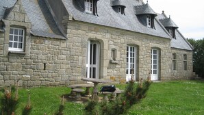 A stone building with a steeply pitched roof, multiple chimneys, and a small front porch with a bench.
