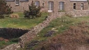 A stone building with a steep roof, a stone staircase leading up to it, and several boats on the grass.