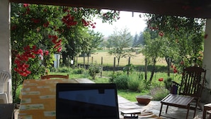 Una computadora portátil sobre una mesa con mantel amarillo, rodeada de sillas y vista a un jardín.
