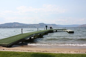A pier extending into a lake with a grassy platform, surrounded by mountains.