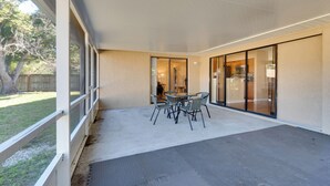 Een terras buiten met een tafel en stoelen, een overdekte doorgang en uitzicht op de achtertuin.