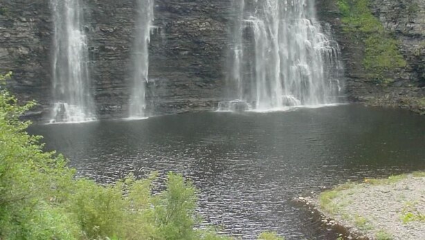 A waterfall cascading into a calm pool surrounded by rocky cliffs and greenery.