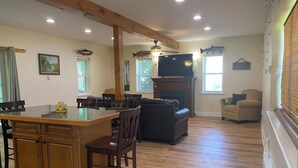 A spacious living area with a wooden floor, a fireplace, a television, and a dining area with a glass-top table and chairs.