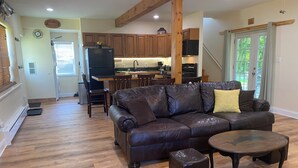 A spacious living room with a leather sofa, a coffee table, and a dining area with wooden cabinets and a kitchen in the background.