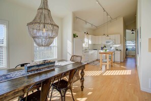 A spacious kitchen with white cabinets, a wooden dining table, and a large chandelier.