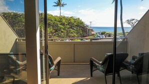 A balcony with wicker chairs, a view of a beach, and a palm tree. - Stunning Ocean Views Steps from Sugar Beach (Kihei)