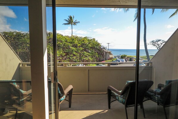 A balcony with wicker chairs, a view of a beach, and a palm tree.