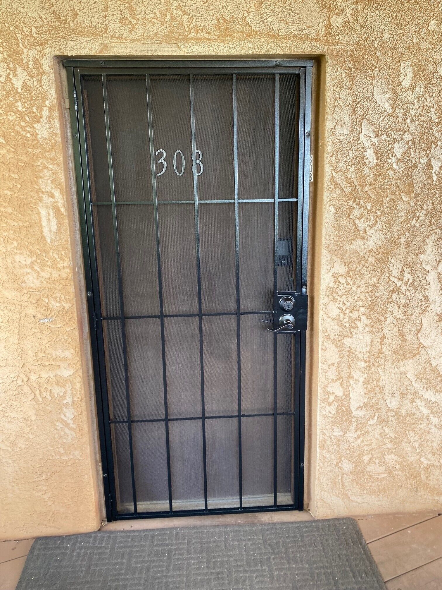 A black metal door with the number 308, a keypad lock, and a textured beige wall.