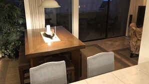 A dining area with a table, chairs, a hanging lamp, and a view through a sliding glass door to an outdoor patio. - Stunning Ocean Views Steps from Sugar Beach (Kihei)