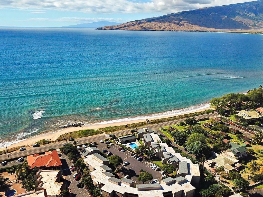 An aerial view of a coastal area with a beach, a road, and buildings.