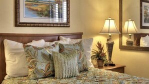 A neatly made bed with patterned bedding and pillows, a bedside lamp, a small potted plant, and a framed picture on the wall. - Gorgeous Oceanview Condo (Ormond Beach)