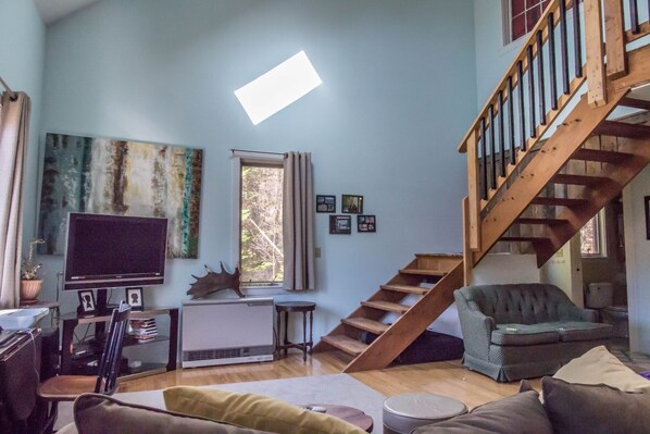 Ein Wohnzimmer mit Fernseher, einer Couch, einer Treppe und einem Fenster mit Vorhängen.