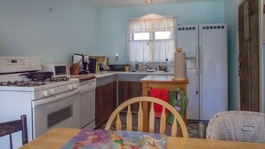 Une cuisine compacte équipée d’une cuisinière, d’un four à micro-ondes et d’un réfrigérateur. On y trouve une table à manger avec des chaises, ainsi qu’une fenêtre avec des rideaux.