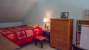 Une chambre à coucher comprenant un lit, une table de chevet, une commode, une lampe, un cadre photo et une bibliothèque.