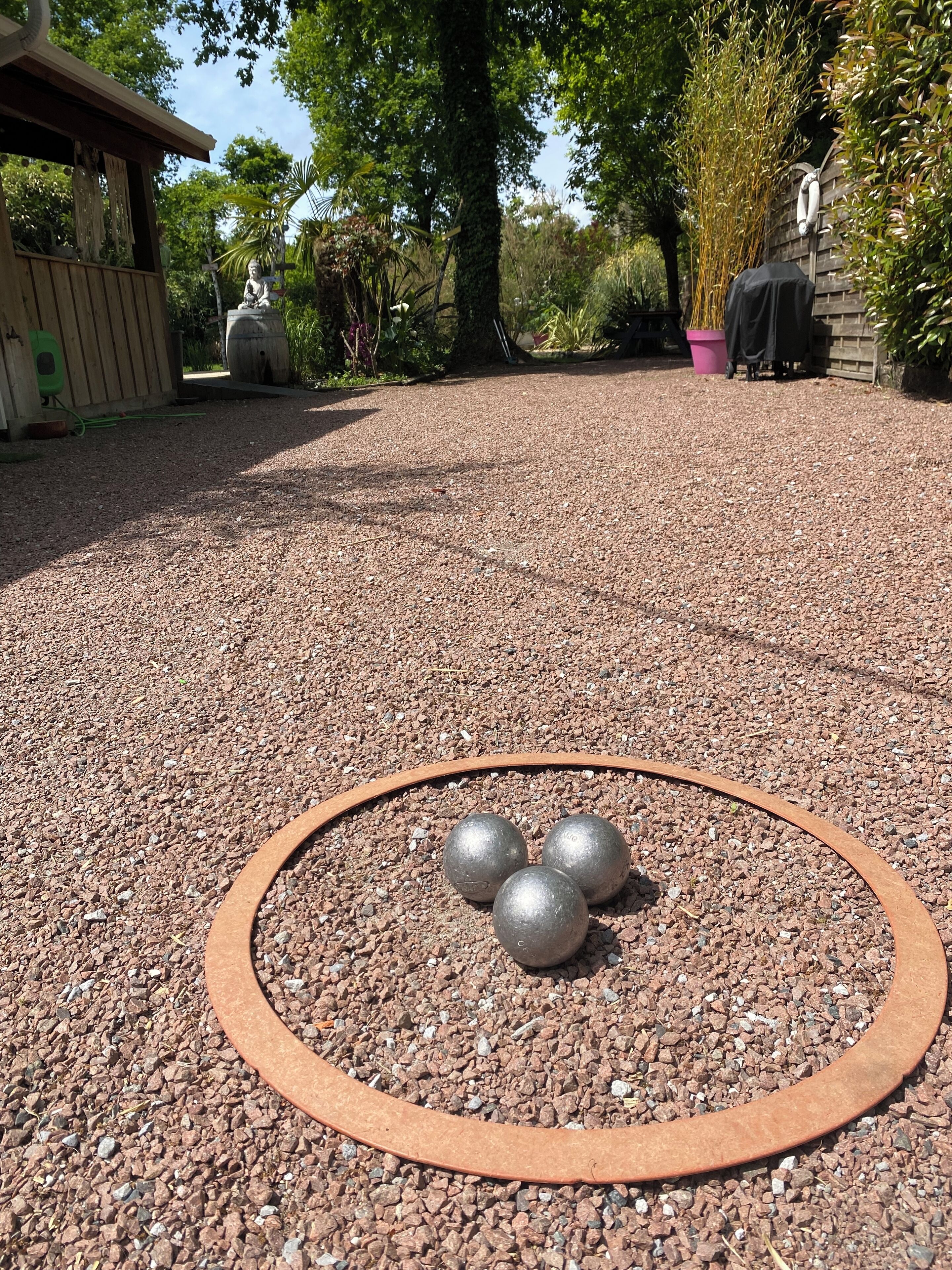 A gravel area with a circular metal frame and three metallic balls.