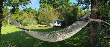 A hammock tied between trees in a lush garden with a wooden deck.