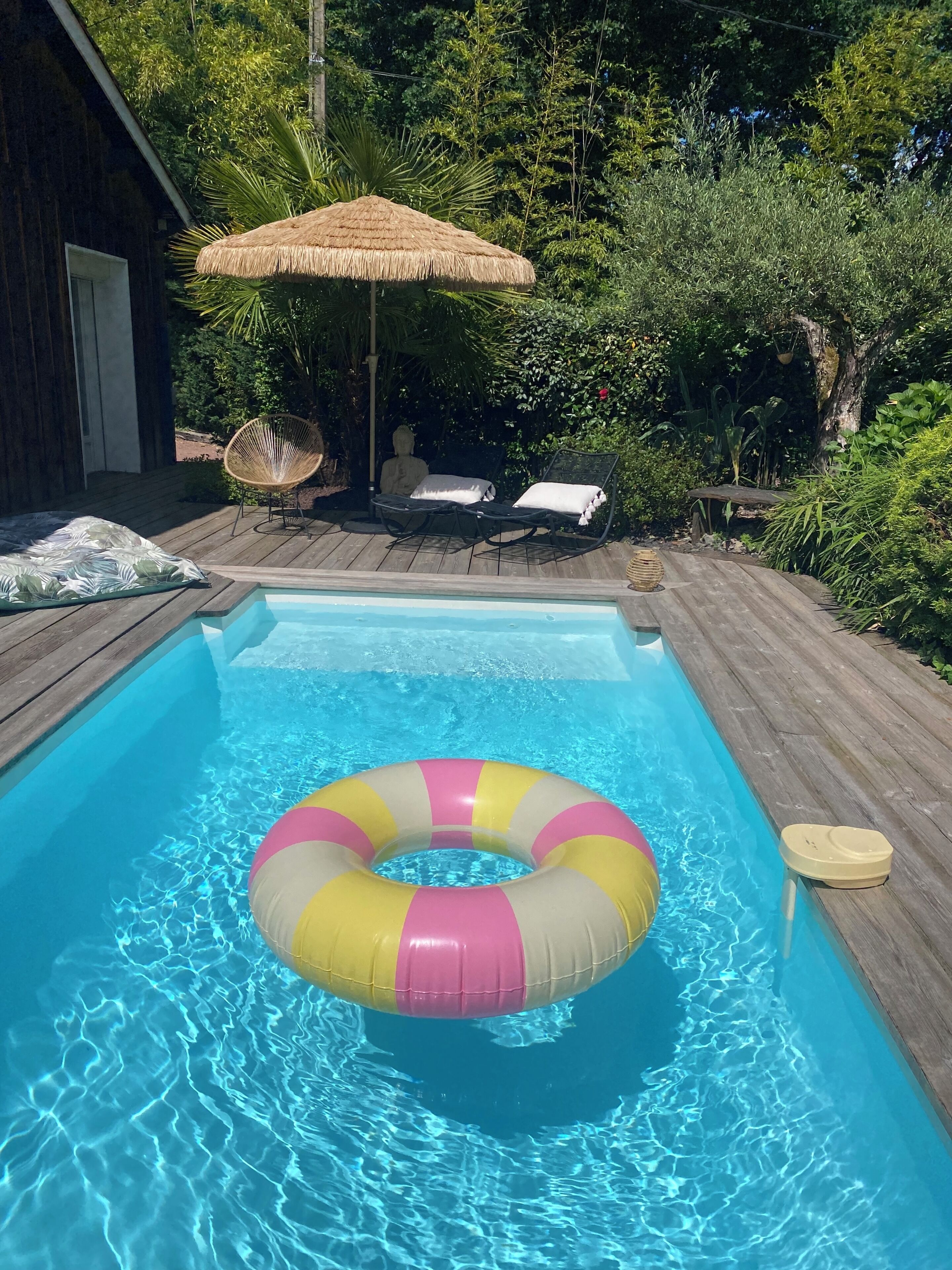 A swimming pool with a floating ring, lounge chairs, and a thatched umbrella.