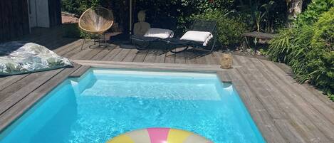 A swimming pool with a floating ring, lounge chairs, and a thatched umbrella.
