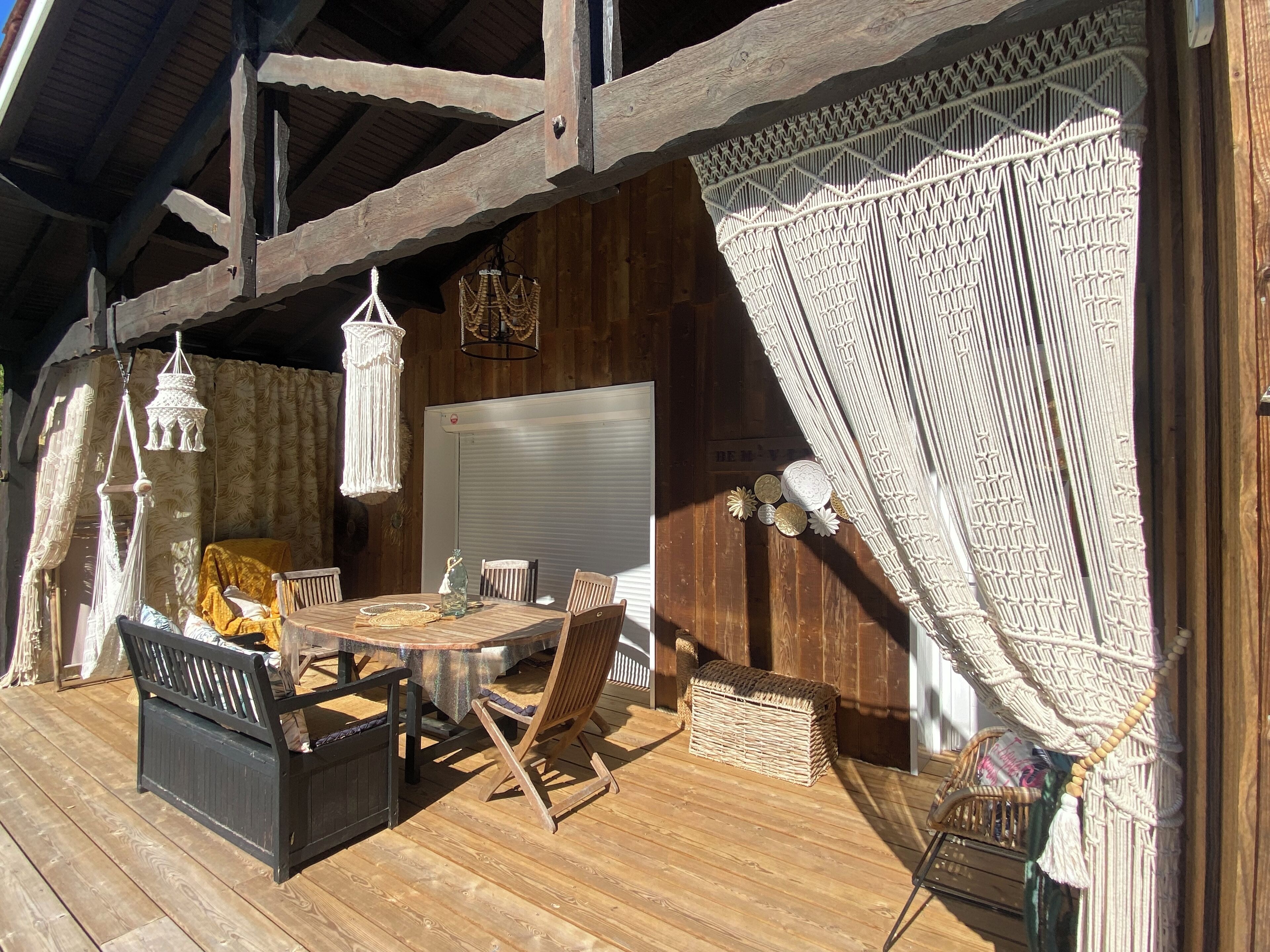 Une terrasse en bois avec une table ronde et des chaises, un banc et un panier en osier.